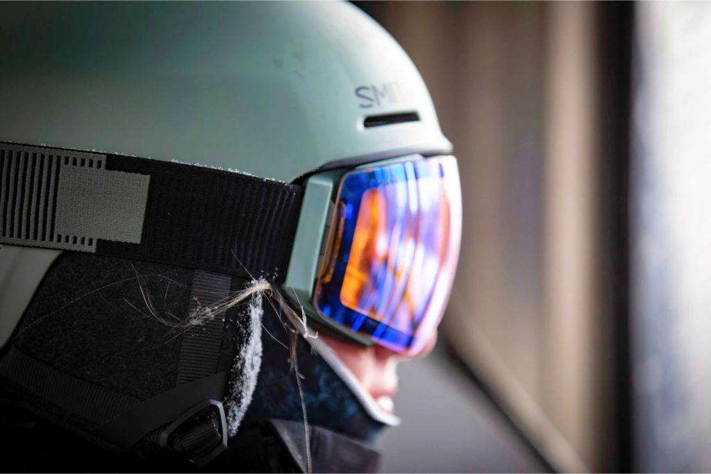 A close-up view of a Smith Vantage helmet's earpad being unzipped to show the installation of a circular Bluetooth audio speaker
