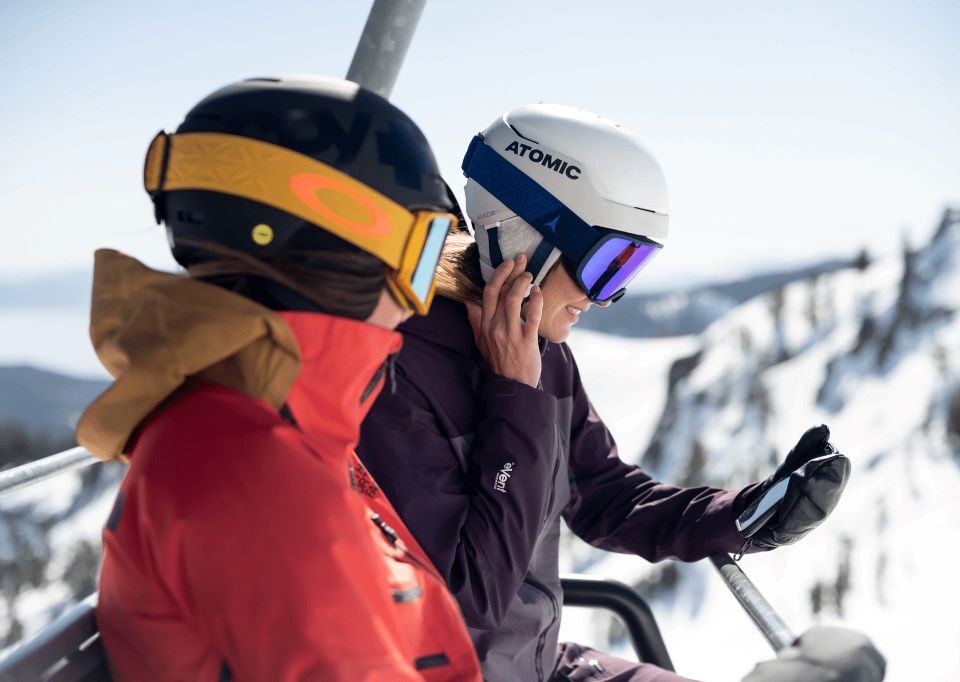 A snowboarder wearing a Smith Vantage helmet smiles on a chairlift while listening to music through integrated helmet audio