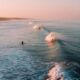 1. Surfer paddling out at remote beach break with pristine waves and empty lineup during golden hour