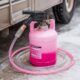Hand-operated antifreeze pump connected to pink RV antifreeze container with clear vinyl tubing for camper winterization