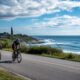 Cyclists riding along coastal road near Twin Lights lighthouse with ocean views in background