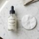 Minimalist dropper bottle and cotton pad on a neutral countertop.